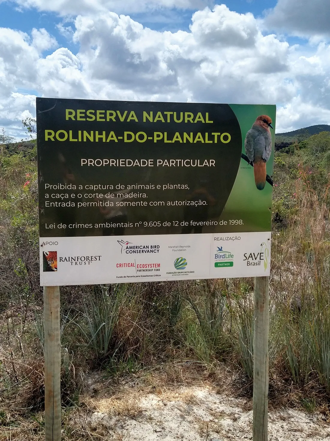 Un panneau d'entrée de la réserve naturelle Rolinha-do-planalto, planté dans une végétation basse.